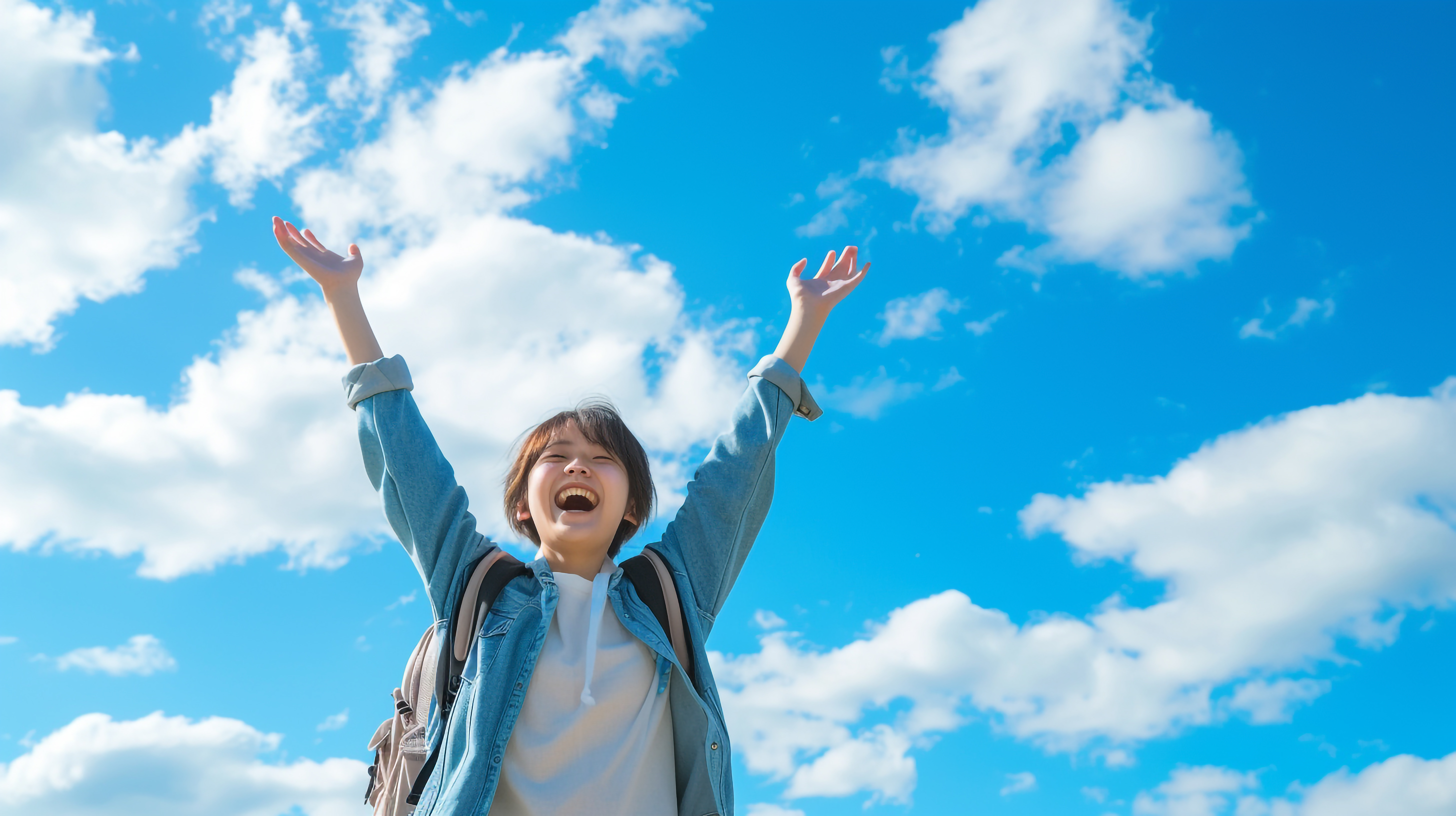 青空の下で両手をあげる高校生