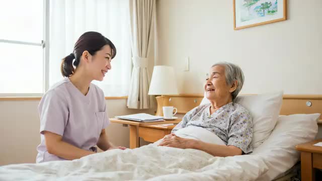 ベッドで介護師の女性と笑顔で会話する高齢女性
